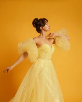 Profile portrait of a beautiful middle-aged woman in a yellow dress, her hair pulled up against a yellow background.