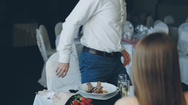 Young bearded man in white shirt is arguing with his girlfriend while dining in restaurant then leaving. Lovers quarrel, negative emotions and relationship crisis concept.
