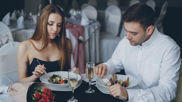 Happy young people are eating salad in luxurious restaurant. Romantic relationships and fine dining concept.