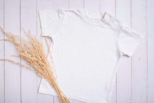 White children's t-shirt mockup for logo, text or design on wooden background with pampas grass top view.