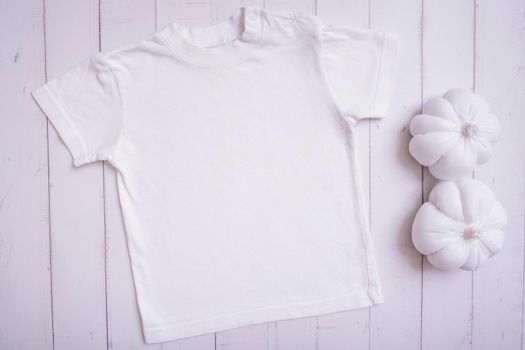 White children's t-shirt mockup for logo, text or design on wooden background with pumpkins top view.