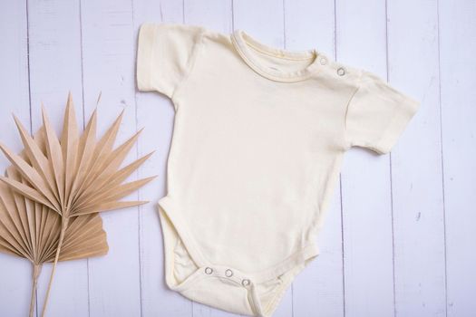 Yellow baby bodysuit mockup for logo, text or design on wooden background with palm leaves top view.