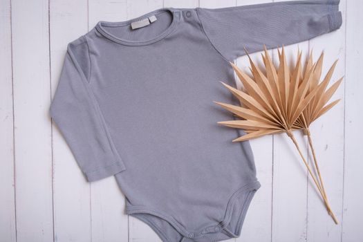 Grey baby bodysuit mockup for logo, text or design on wooden background with palm leaves top view.