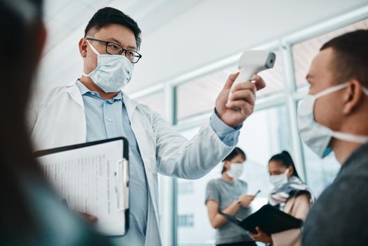 Doctor testing covid temperate in hospital appointment to prevent the spread of the virus. Healthcare compliance worker with health insurance document and face mask checking or scanning patient head.