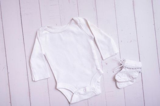 White baby bodysuit mockup for logo, text or design on wooden background top view.
