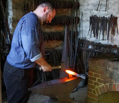 Detmold, NRW, Germany - July 19 2017 A strong built blacksmith shows his work in an open-air museum. He is hammering red-hot iron.