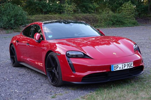 Rheine, NRW, Germany - August 24 2022 A red Porsche Taycan parked on gravel. This is an electric sedan and Porsche's first series-produced electric car