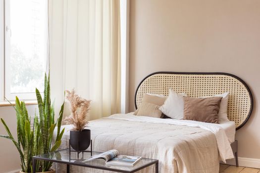 Table and potted plant placed near comfortable bed and staircase in spacious bedroom in modern apartment