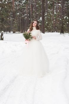 Beautiful bride in a white dress with a bouquet in a snow-covered winter forest. Portrait of the bride in nature.