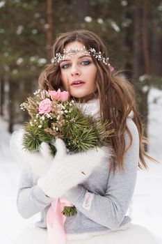 Beautiful bride in a white dress with a bouquet in a snow-covered winter forest. Portrait of the bride in nature.