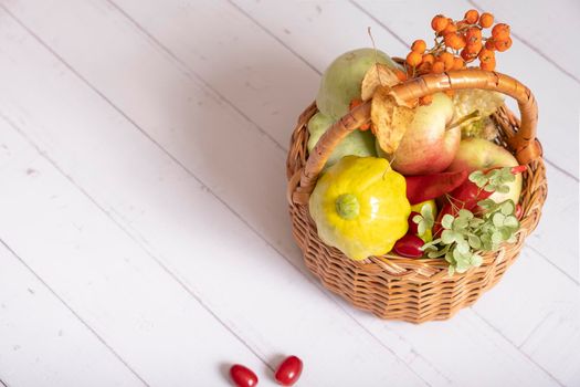 Autumn harvest basket with corn, apples, zucchini and peppers on a wooden background decorated with autumn leaves and mountain ash