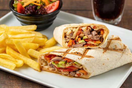 Meat wrap cut in half with french fries on dark stone table