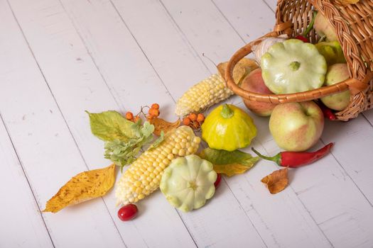 Autumn harvest basket with corn, apples, zucchini and peppers on a wooden background decorated with autumn leaves
