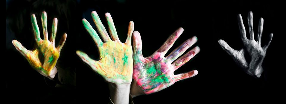 Close up shot of hands of children with some paint over it isolated over a black background, horizontal shot.