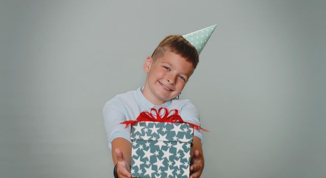 Smiling toddler young boy presenting birthday gift box stretches out hands, offer wrapped present career bonus, celebrating party. School children teenager. Child isolated on gray studio background