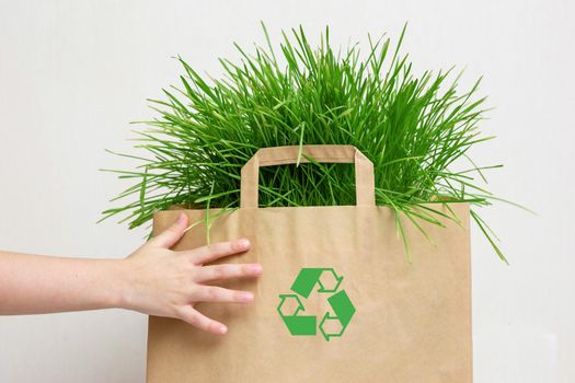 Kids hands hold a paper bag with green grass. Close. Layout. Copy space. The concept of recycling and environmental protection.