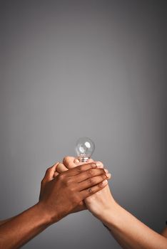 Light up someone elses day. Studio shot of unidentifiable hands holding a light bulb against a gray background