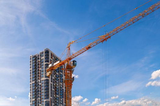 freshly built high rise apartment building near yellow crane on blue sky background with thin feathery clouds.