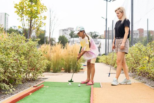 Detail of young woman and daughter playing mini adventure golf on a beautiful sunny summer day.