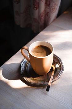 A cup of coffee on vintage matal plate on white wooden table at morning light, selective focus, copy space.