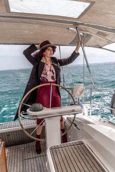 Attractive middle-aged woman at the helm of a yacht on a summer day. Luxury summer adventure, outdoor activities