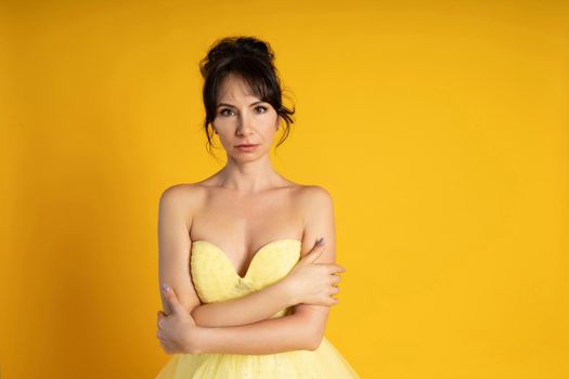 Portrait of a beautiful middle-aged woman in a yellow dress, her hair pulled up against a yellow background.