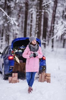 A woman in a winter snow-covered forest in the trunk of a car decorated with Christmas decor. A female photographer holds a camera in her hands.