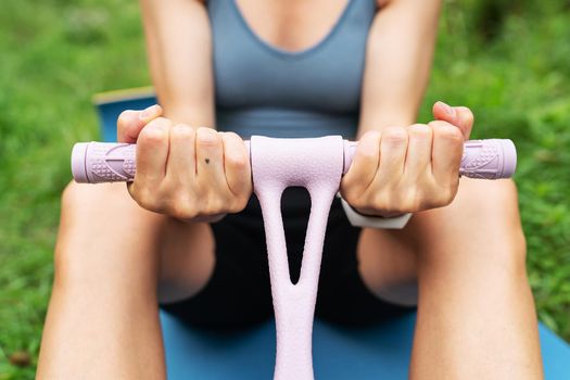 Athletic girl doing exercises on a hand trainer in nature outdoors on a blurred background. A woman is doing yoga in the park, sitting on the grass