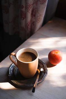 A cup of coffee on vintage matal plate on white wooden table with a peach in the interior, summer morning concept, selective focus, copy space.