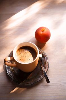 A cup of coffee on vintage matal plate on white wooden table with a peach, top view, summer morning concept, selective focus, copy space.