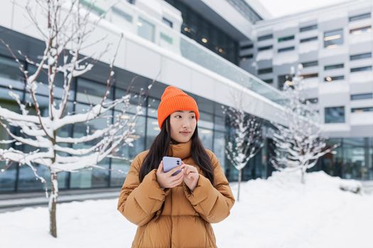 Beautiful Asian girl uses the phone, online dating, makes a choice, walks on a winter snowy day