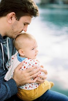 Dad hugs a baby sitting on his lap and kisses him on the top of his head. High quality photo