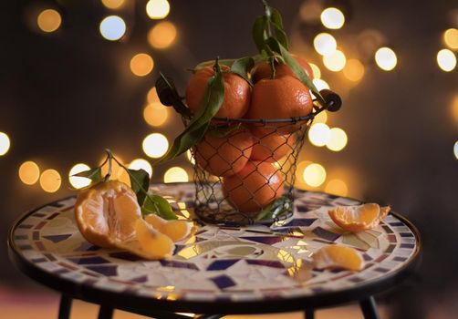 tangerines in a mesh bucket on a table against a background of bright yellow bokeh, New Year's mood. High quality photo