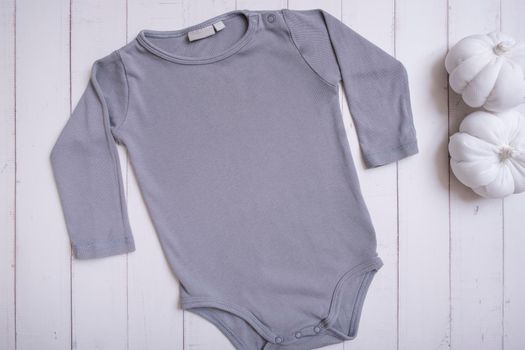 Grey baby bodysuit mockup for logo, text or design on wooden background with pumpkins top view.