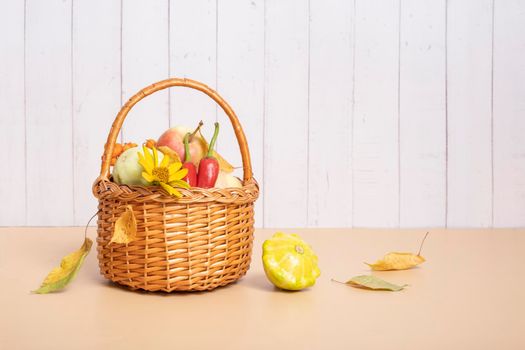 Autumn harvest basket with corn, apples, zucchini and peppers on a wooden background decorated with autumn flower.