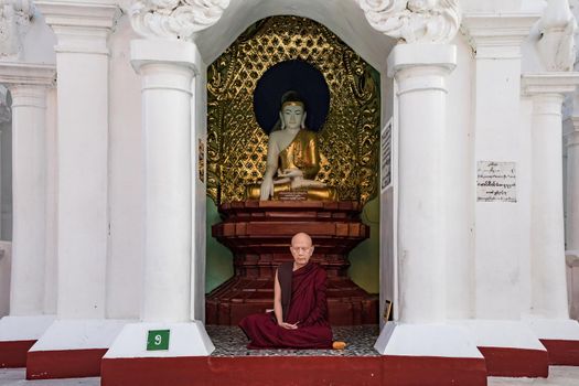 A monk meditating in front of a Buddha statue in Yangon