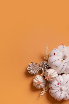 White decorative hand made pumpkins with shiny stones and pine cones on colored background. Thanksgiving day concept. Copy space
