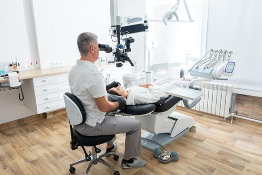 Male dentist using dental microscope treating patient teeth at dental clinic office. Medicine, dentistry and health care concept