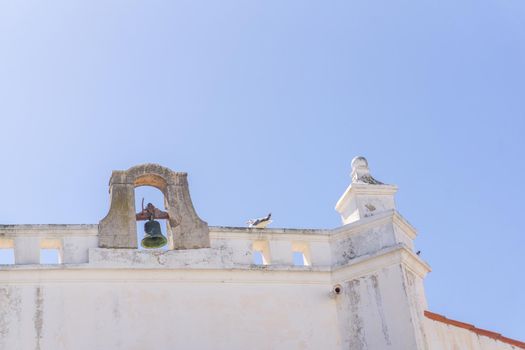 Bell on the roof of an old Portuguese Catholic church on a sunny day against the sky