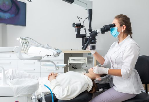 Female dentist using dental microscope treating patient teeth at dental clinic office. Medicine, dentistry and health care concept