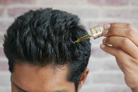 young men applying essential oils on his hair .