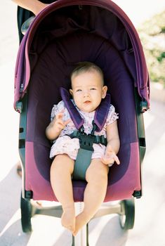Baby sits in a stroller with a seatbelt in the street. High quality photo