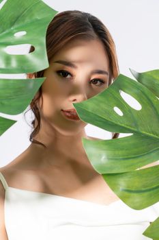 Closeup portrait of young gorgeous woman with healthy fair skin holding big green leaf near her face. Skin care beauty care concept.