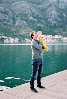 Dad hugs and kisses a baby in his arms while standing on the pier. High quality photo