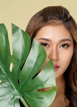 Closeup portrait of young ardent woman with healthy fair skin holding big green leaf near her face. Skin care beauty care concept.