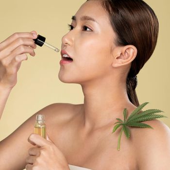 Closeup portrait of young ardent woman with healthy fresh skin taking cbd oil with hemp leaf. Combination of beauty and cannabis concept.