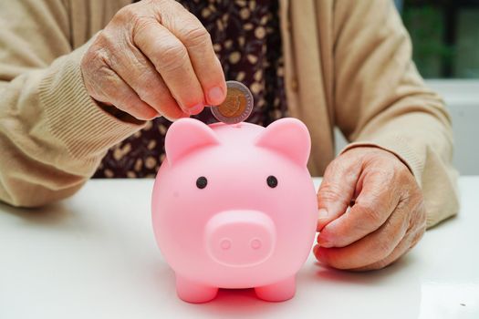 Retired elderly woman putting coins money in piggy bank and worry about monthly expenses and treatment fee payment.