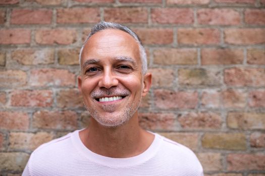 Portrait of smiling caucasian adult man wearing pink sweater looking at camera. Orange brick wall background. Lifestyle concept.