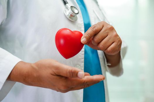 Asian woman doctor holding red heart for health in hospital.