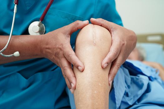 Doctor checking Asian elderly woman patient with scar knee replacement surgery in hospital.